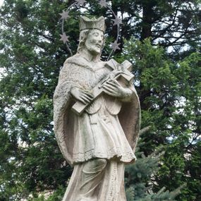 Zdjęcie nr 1: Na dwóch stopniach ustawiono wysoki cokół zwieńczony gzymsem, na którym na podstawie znajduje się figura św. Jana Nepomucena. Z czterech stron cokołu są fakturowane płyciny, na przedniej wyryto datę 1779. Święty o esowato wygiętej sylwetce, w kontrapoście, z prawą nogą zgiętą w kolanie. W obu rękach trzyma krucyfiks. Ma podłużną twarz okoloną krótkim zarostem i długimi, spływającymi na kark włosami. Ma półprzymknięte oczy, mały, wąski nos i rozciągnięte w delikatnym uśmiechu usta. Jest ubrany w strój kanonika: ma narzuconą na sutannę i komżę futrzaną almucję, a na głowie biret. Wokół głowy nimb z sześcioma gwiazdkami. 