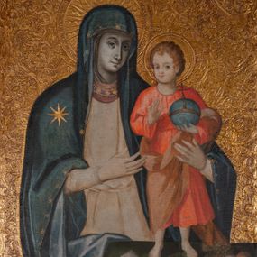 Zdjęcie nr 1: Obraz w kształcie stojącego prostokąta z wizerunkiem Maki Boskiej z Dzieciątkiem. Maria została przedstawiona w pozycji stojącej, frontalnie, przytrzymuje Dzieciątko lewą ręką, a prawą na nie wskazuje. Patrzy na widza, ma pogodny wyraz twarzy, ciemne oczy, prosty nos i małe usta. Jest ubrana w białą suknię z pasem haftu pod szyją i granatowy maforion zdobiony złotą gwiazdą na prawym ramieniu i delikatnym ornamentem na brzegach. Dzieciątko patrzy na widza, unosi prawą dłoń w geście błogosławieństwa, w lewej trzyma niebieską kulę ze złotą opaską zwieńczoną krzyżem. Ma owalną twarz z wysokim czołem, głęboko osadzonymi oczami, szerokim nosem i małymi ustami. Jest ubrane w czerwoną sukienkę i jasnobrązowy płaszcz, który owija się wokół jego prawego biodra i przechodzi przez lewą rękę, stopy ma bose. Młody Jezus stoi na stole nakrytym ciemnozieloną tkaniną. Przed nim po lewej stronie leży otwarta księga z zapisanymi stronami, po prawej patera z owocami. Nimby wyciskane, promieniste, obwiedzione kolistym otokiem, złocone. Tło również złote, wyciskane w gęsty ornament roślinno-kwiatowy, z drobnych form oplecionych wijącą się łodygą. 