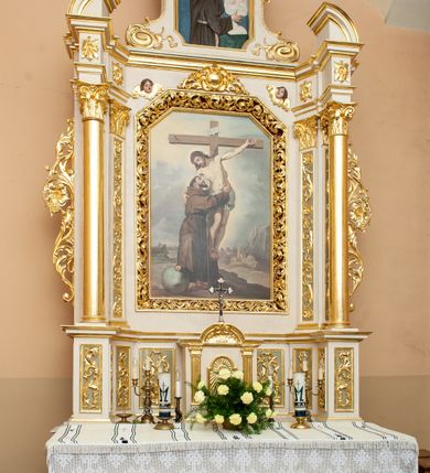 Zdjęcie nr 5: Ołtarz architektoniczny, przyścienny, jednokondygnacyjny, jednoosiowy ze zwieńczeniem. Mensa w typie sarkofagowym, na wysokim cokole, gładka, górna partia cokołu oddzielona profilowanymi listwami. Na mensie ustawiono tabernakulum w formie prostopadłościennej szafki, ze ścianką frontową ujętą kanelowanymi pilastrami jońskimi wspierającymi gzyms, pośrodku przyczółek utworzony z dwóch stykających się wolut, wypełniony muszlą. Drzwiczki w kształcie stojącego prostokąta zamknięte łukiem półkolistym nadwieszonym z przedstawieniem kielicha z hostią. 
Nastawa ustawiona na wysokim cokole ujęta parami pilastrów, z których wewnętrzne ustawione ukośnie oraz stojącymi na ich tle kolumnami, podtrzymującymi odcinki belkowania oraz fragmenty naczółków. Pole środkowe z wnęką w kształcie stojącego prostokąta o ściętych górnych narożach, ujęte ozdobną ramą wypełnioną ażurowym ornamentem akantowym. W niej obraz z przedstawienie św. Franciszka obejmującego ukrzyżowanego Chrystusa. Pola cokołów i pilastrów są wypełnione stylizowaną wicią akantu, boki ołtarza flankowane ażurową wicią akantową z rozetą. Zwieńczenie ujęte spływami wolutowymi, zakończone gzymsem w kształcie łuku półkolistego nadwieszonego. W zwieńczeniu płaskorzeźbione przedstawienie św. Antoniego Padewskiego w prostokątnej ramie o ściętych ćwierćkoliście dolnych narożach i zakończonej łukiem nadwieszonym z uskokiem. Całość struktury ołtarza polichromowana w kremowym odcieniu, wnętrza płycin szare, detal architektoniczny i ornamenty pozłacane.