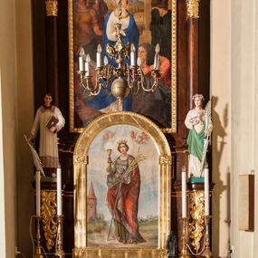 Zdjęcie nr 1: Ołtarz przyścienny, architektoniczny, jednoosiowy, jednokondygnacyjny ustawiony na jednym stopniu. Mensa prostopadłościenna, skrzyniowa, z antepedium ujętym po bokach kanelowanymi pilastrami, dzielonym płaskimi listwami na trzy pola. W środkowym, najszerszym aplikowany płaskorzeźbiony Baranek Boży leżący na księdze, z chorągwią, w polach bocznych płaskorzeźbiony motyw krzyża uformowanego z liści akantu. Nastawa na wysokim, dwudzielnym cokole, przedzielona wystającym gzymsem. Boczne osie wysunięte do przodu, dekorowane ornamentem roślinnym, stanowią konsole pod rzeźby św. Szczepana po lewej stronie i św. Agnieszki po prawej. Między nimi obraz w kształcie stojącego prostokąta zamknięty od góry łukiem półkolistym z przedstawieniem św. Barbary. Nastawa ołtarzowa w formie arkady zamkniętej łukiem półkolistym, wspartym na dwóch kolumnach o kapitelach dekorowanych ornamentem roślinnym. Łuk ozdobiony innym płaskorzeźbionym ornamentem roślinnym, zwieńczony krzyżem o ramionach zakończonych trójlistnie. W polu środkowym obraz w kształcie stojącego prostokąta, zamknięty półkoliście z przedstawieniem św. Katarzyny (?). Całość struktury ołtarza bejcowana na kolor ciemnobrązowy, detal architektoniczny złocony, polichromia rzeźb w partiach ciała naturalistyczna. 