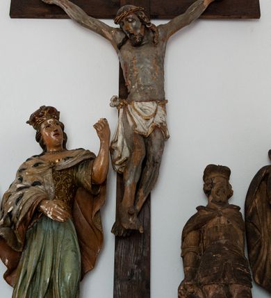 Zdjęcie nr 1: Pełnoplastyczna figura Chrystusa przybitego do krzyża trzema gwoździami. Ciało zwisa wyprężone, korpus sztywny, kolana odchylone na prawo, palce rąk częściowo przykurczone. Głowa Chrystusa opada na jego prawy bark. Ma pociągłą twarz, oczy zamknięte, usta rozchylone. Okala ją krótka, ciemnobrązowa broda i długie włosy zwinięte w pukle, opadające na plecy i barki; na głowie cienka korona cierniowa. Widoczne ślady męki, spod korony, w miejscach przebicia gwoździami i w boku zaznaczono strugi spływającej krwi. Biodra okrywa perizonium w formie białej tkaniny lamowanej złotem, przewiązanej grubym sznurem związanym na prawym biodrze. Na górnej belce krzyża, na kartuszu utworzonym z ornamentu małżowinowo-chrząskowego inskrypcja „INRI”. 