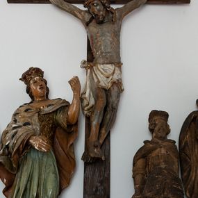 Zdjęcie nr 1: Pełnoplastyczna figura Chrystusa przybitego do krzyża trzema gwoździami. Ciało zwisa wyprężone, korpus sztywny, kolana odchylone na prawo, palce rąk częściowo przykurczone. Głowa Chrystusa opada na jego prawy bark. Ma pociągłą twarz, oczy zamknięte, usta rozchylone. Okala ją krótka, ciemnobrązowa broda i długie włosy zwinięte w pukle, opadające na plecy i barki; na głowie cienka korona cierniowa. Widoczne ślady męki, spod korony, w miejscach przebicia gwoździami i w boku zaznaczono strugi spływającej krwi. Biodra okrywa perizonium w formie białej tkaniny lamowanej złotem, przewiązanej grubym sznurem związanym na prawym biodrze. Na górnej belce krzyża, na kartuszu utworzonym z ornamentu małżowinowo-chrząskowego inskrypcja „INRI”. 