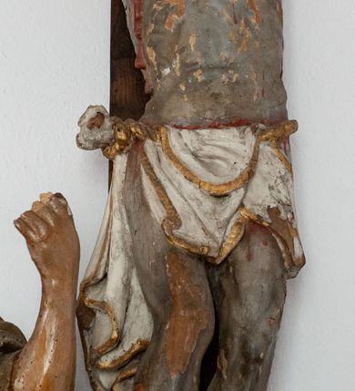 Zdjęcie nr 2: Pełnoplastyczna figura Chrystusa przybitego do krzyża trzema gwoździami. Ciało zwisa wyprężone, korpus sztywny, kolana odchylone na prawo, palce rąk częściowo przykurczone. Głowa Chrystusa opada na jego prawy bark. Ma pociągłą twarz, oczy zamknięte, usta rozchylone. Okala ją krótka, ciemnobrązowa broda i długie włosy zwinięte w pukle, opadające na plecy i barki; na głowie cienka korona cierniowa. Widoczne ślady męki, spod korony, w miejscach przebicia gwoździami i w boku zaznaczono strugi spływającej krwi. Biodra okrywa perizonium w formie białej tkaniny lamowanej złotem, przewiązanej grubym sznurem związanym na prawym biodrze. Na górnej belce krzyża, na kartuszu utworzonym z ornamentu małżowinowo-chrząskowego inskrypcja „INRI”. 