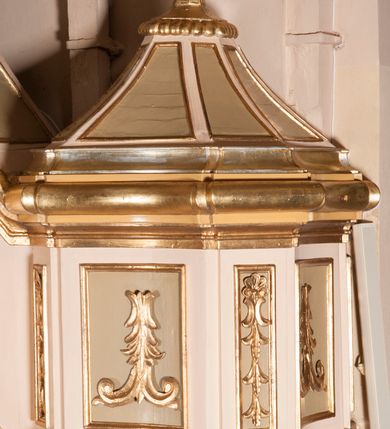 Zdjęcie nr 2: Ambona przyścienna składająca się z kosza, zaplecka, baldachimu i schodów z balustradą, zawieszona na lewej ścianie prezbiterium. Kosz na planie ośmioboku, o ściankach naprzemiennie prostych i wklęsłych, dekorowanych płycinami z plakietami ornamentalnymi. Podstawa kosza stożkowa, z wypełniającymi płaszczyzny płycinami, z pozłacaną szyszką u dołu. Zaplecek w kształcie prostokąta z prostokątną płyciną, wewnątrz której aplikowany stylizowany ornament roślinny i dwie główki anielskie poniżej łuku trójlistnego. Baldachim powtarzający plan kosza, ujęty profilowanym gzymsem, wyłamanym w narożach, z podwieszonym lambrekinem i zwieńczony rzędem ornamentu złożonego ze stylizowanych lilii.  Baldachim wieńczy pełnoplastyczna figura Chrystusa Zmartwychwstałego ustawiona na stożkowej podstawie. Chrystus został ukazany w całej postaci, z prawą ręką uniesioną w geście błogosławieństwa, lewą przytrzymując płaszcz. Ma owalną twarz okoloną długimi włosami, które spływają mu na ramiona i plecy. Wokół bioder ma obwiązane białe perizonium, na plecach zarzucony złoty płaszcz spięty na dekolcie; szaty łamią się ostrymi fałdami. W podniebiu baldachimu znajduje się rzeźba srebrnej gołębicy Ducha Świętego. Balustrada z profilowaną poręczą, artykułowana romboidalnymi płycinami  z plakietami. Kolorystyka pastelowa, jasna. Struktura w kolorze kremowym, płyciny jasnoszare, fryz baldachimu bordowy detal architektoniczny i ornamenty pozłacane. 