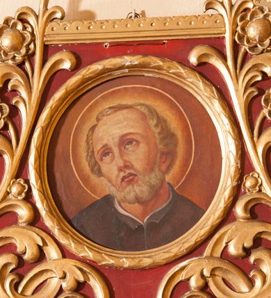 Zdjęcie nr 1: Przedstawienie stanowi jedynie portret świętego, który ma głowę przechyloną na prawo i wzrok skierowany do góry. Bobola ma prostokątną twarz, uniesione brwi, wąski nos i ledwie zaznaczone, zamknięte usta; twarz okala siwa broda, krótkie włosy są zaczesane na boki i do tyłu. Pod szyją widać kawałek czarnej, rozciętej sutanny nałożonej na białą koszulę. Tło jest jednolite, brązowe, jaśniejące wokół głowy świętego otoczonej nimbem. Okrągły obraz ujęto ramką utworzoną z liści laurowych umieszczoną w rozbudowanym obramowaniu w kształcie zbliżonym do stojącego prostokąta o zaoblonych dołem krawędziach. Wypełniają je wychodzące od centralnie umieszczonej palmety sploty płaskorzeźbionej, złotej wici roślinnej z rozwiniętymi kwiatami umieszczone na bordowym tle; górna krawędź dekorowana koronką. 
