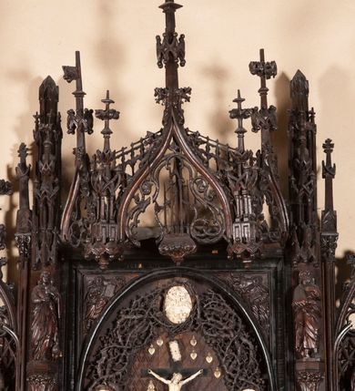 Zdjęcie nr 4: Ołtarz architektoniczny, dwukondygnacyjny ze zwieńczeniem, trójosiowy. Neogotycki na trapezowym postumencie. Mensa wsparta na dwóch  kolumnach o schodkowych, bazach w formie ośmioramiennych gwiazd na siedmiobokach z wklęsłymi ramionami. Z każdego ramienia gwiazd strzeliście unosiła się ku kapitelowi wzdłuż trzonu służka, tworząc u dołu romboidalną, wklęsłą siatkę. Struktura ta zachowała się mniej niż  w połowie na lewej kolumnie. Kapitel lewy ornamentalnie pokryty regularną siatką ze stylizowanych, suchych gałęzi, które tworzą trzy strefy pól ornamentalnych. Dolne przypominają ostre łuki, krzyżują się w nich gałęzie. Środkowe, romboidalne są puste a górne wypełniają sploty suchego akantu. Prawy kapitel posiada podobne podziały pól, różni się wypełnieniem górnej ze stref, gdzie przestrzeń całkowicie zajmują na przemian bujne winne grona oraz pochylające się kłosy zbóż. Zaplecek pod mensą, od frontu podzielono na sześć stref. Na dwóch zewnętrznych i dwóch środkowych znajdują się przedstawienia płaskorzeźbionych łuków okiennych z maswerkami. Druga płaszczyzna od lewej i prawej ozdobiona jest płaskorzeźbą roślinną. Ryzalitowana w części środkowej kondygnacja pierwsza stanowi tabernakulum na cokole. Zadaszenie spadziste pokryte różnorodnym zdobieniem, flankowane czworokątnymi filarami, na których kapitelach wspierają się ramiona ostrych łuków z wimpergami. Powyżej kapitele filarów stanowią blanki z których wyrastają ażurowe formy zbudowane z kilku esownic stylizowane na oset, zakończone profitkami. Widać wnętrze tabernakulum przez ażurowe, dwuskrzydłowe drzwiczki. Na lewych jest przestrzenna rzeźba Orła w koronie osadzona w nieznacznie uszkodzonej oprawie ze splotów gałęzi. Z prawej podobnie wykonane przedstawienie Pogoni Litewskiej. Konny rycerz ma złamany miecz. W centrum ołtarza w prostokątnej ramie znajduje się owalne pole wewnątrz otoczone ciasnym splotem guzowatych gałęzi. W środkowych punktach owalu z gałęzi wstawiono owalne  płaskorzeźby z kości słoniowej ze scenami z życia Chrystusa. W samym środku niewielka rzeźba Jezusa Ukrzyżowanego. Ramę główną flankują postacie Ewangelistów po dwóch z każdej strony, jeden nad drugim, na postumentach i pod gotyckimi baldachimami, najwyższy jest okazalszy. Zwieńczenie ołtarza stanowi wysunięta balustrada zbudowana z ostrołukowych ramion ze sterczynami, centralne ramiona zbiegają się i łączą w sterczynę zakończoną krzyżem. Ołtarz flankowany strzelistymi formami z typowych dla neogotyckiej stylizacji elementami architektonicznymi, w które wkomponowano po jednej postaci świętych z każdej strony.