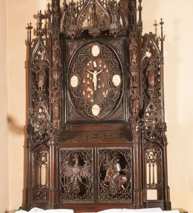 Zdjęcie nr 1: Ołtarz architektoniczny, dwukondygnacyjny ze zwieńczeniem, trójosiowy. Neogotycki na trapezowym postumencie. Mensa wsparta na dwóch  kolumnach o schodkowych, bazach w formie ośmioramiennych gwiazd na siedmiobokach z wklęsłymi ramionami. Z każdego ramienia gwiazd strzeliście unosiła się ku kapitelowi wzdłuż trzonu służka, tworząc u dołu romboidalną, wklęsłą siatkę. Struktura ta zachowała się mniej niż  w połowie na lewej kolumnie. Kapitel lewy ornamentalnie pokryty regularną siatką ze stylizowanych, suchych gałęzi, które tworzą trzy strefy pól ornamentalnych. Dolne przypominają ostre łuki, krzyżują się w nich gałęzie. Środkowe, romboidalne są puste a górne wypełniają sploty suchego akantu. Prawy kapitel posiada podobne podziały pól, różni się wypełnieniem górnej ze stref, gdzie przestrzeń całkowicie zajmują na przemian bujne winne grona oraz pochylające się kłosy zbóż. Zaplecek pod mensą, od frontu podzielono na sześć stref. Na dwóch zewnętrznych i dwóch środkowych znajdują się przedstawienia płaskorzeźbionych łuków okiennych z maswerkami. Druga płaszczyzna od lewej i prawej ozdobiona jest płaskorzeźbą roślinną. Ryzalitowana w części środkowej kondygnacja pierwsza stanowi tabernakulum na cokole. Zadaszenie spadziste pokryte różnorodnym zdobieniem, flankowane czworokątnymi filarami, na których kapitelach wspierają się ramiona ostrych łuków z wimpergami. Powyżej kapitele filarów stanowią blanki z których wyrastają ażurowe formy zbudowane z kilku esownic stylizowane na oset, zakończone profitkami. Widać wnętrze tabernakulum przez ażurowe, dwuskrzydłowe drzwiczki. Na lewych jest przestrzenna rzeźba Orła w koronie osadzona w nieznacznie uszkodzonej oprawie ze splotów gałęzi. Z prawej podobnie wykonane przedstawienie Pogoni Litewskiej. Konny rycerz ma złamany miecz. W centrum ołtarza w prostokątnej ramie znajduje się owalne pole wewnątrz otoczone ciasnym splotem guzowatych gałęzi. W środkowych punktach owalu z gałęzi wstawiono owalne  płaskorzeźby z kości słoniowej ze scenami z życia Chrystusa. W samym środku niewielka rzeźba Jezusa Ukrzyżowanego. Ramę główną flankują postacie Ewangelistów po dwóch z każdej strony, jeden nad drugim, na postumentach i pod gotyckimi baldachimami, najwyższy jest okazalszy. Zwieńczenie ołtarza stanowi wysunięta balustrada zbudowana z ostrołukowych ramion ze sterczynami, centralne ramiona zbiegają się i łączą w sterczynę zakończoną krzyżem. Ołtarz flankowany strzelistymi formami z typowych dla neogotyckiej stylizacji elementami architektonicznymi, w które wkomponowano po jednej postaci świętych z każdej strony.