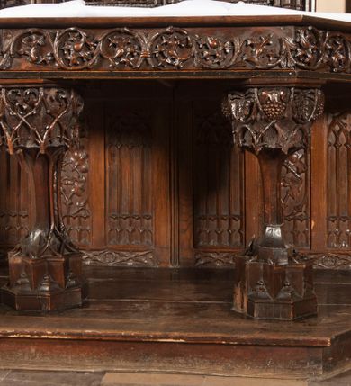 Zdjęcie nr 11: Ołtarz architektoniczny, dwukondygnacyjny ze zwieńczeniem, trójosiowy. Neogotycki na trapezowym postumencie. Mensa wsparta na dwóch  kolumnach o schodkowych, bazach w formie ośmioramiennych gwiazd na siedmiobokach z wklęsłymi ramionami. Z każdego ramienia gwiazd strzeliście unosiła się ku kapitelowi wzdłuż trzonu służka, tworząc u dołu romboidalną, wklęsłą siatkę. Struktura ta zachowała się mniej niż  w połowie na lewej kolumnie. Kapitel lewy ornamentalnie pokryty regularną siatką ze stylizowanych, suchych gałęzi, które tworzą trzy strefy pól ornamentalnych. Dolne przypominają ostre łuki, krzyżują się w nich gałęzie. Środkowe, romboidalne są puste a górne wypełniają sploty suchego akantu. Prawy kapitel posiada podobne podziały pól, różni się wypełnieniem górnej ze stref, gdzie przestrzeń całkowicie zajmują na przemian bujne winne grona oraz pochylające się kłosy zbóż. Zaplecek pod mensą, od frontu podzielono na sześć stref. Na dwóch zewnętrznych i dwóch środkowych znajdują się przedstawienia płaskorzeźbionych łuków okiennych z maswerkami. Druga płaszczyzna od lewej i prawej ozdobiona jest płaskorzeźbą roślinną. Ryzalitowana w części środkowej kondygnacja pierwsza stanowi tabernakulum na cokole. Zadaszenie spadziste pokryte różnorodnym zdobieniem, flankowane czworokątnymi filarami, na których kapitelach wspierają się ramiona ostrych łuków z wimpergami. Powyżej kapitele filarów stanowią blanki z których wyrastają ażurowe formy zbudowane z kilku esownic stylizowane na oset, zakończone profitkami. Widać wnętrze tabernakulum przez ażurowe, dwuskrzydłowe drzwiczki. Na lewych jest przestrzenna rzeźba Orła w koronie osadzona w nieznacznie uszkodzonej oprawie ze splotów gałęzi. Z prawej podobnie wykonane przedstawienie Pogoni Litewskiej. Konny rycerz ma złamany miecz. W centrum ołtarza w prostokątnej ramie znajduje się owalne pole wewnątrz otoczone ciasnym splotem guzowatych gałęzi. W środkowych punktach owalu z gałęzi wstawiono owalne  płaskorzeźby z kości słoniowej ze scenami z życia Chrystusa. W samym środku niewielka rzeźba Jezusa Ukrzyżowanego. Ramę główną flankują postacie Ewangelistów po dwóch z każdej strony, jeden nad drugim, na postumentach i pod gotyckimi baldachimami, najwyższy jest okazalszy. Zwieńczenie ołtarza stanowi wysunięta balustrada zbudowana z ostrołukowych ramion ze sterczynami, centralne ramiona zbiegają się i łączą w sterczynę zakończoną krzyżem. Ołtarz flankowany strzelistymi formami z typowych dla neogotyckiej stylizacji elementami architektonicznymi, w które wkomponowano po jednej postaci świętych z każdej strony.