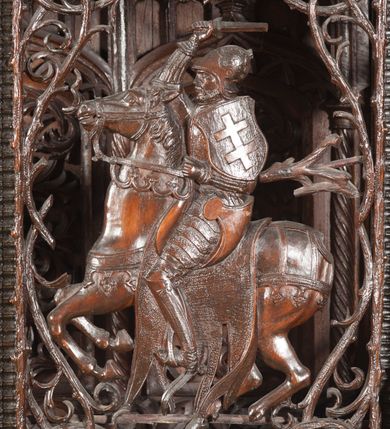 Zdjęcie nr 14: Ołtarz architektoniczny, dwukondygnacyjny ze zwieńczeniem, trójosiowy. Neogotycki na trapezowym postumencie. Mensa wsparta na dwóch  kolumnach o schodkowych, bazach w formie ośmioramiennych gwiazd na siedmiobokach z wklęsłymi ramionami. Z każdego ramienia gwiazd strzeliście unosiła się ku kapitelowi wzdłuż trzonu służka, tworząc u dołu romboidalną, wklęsłą siatkę. Struktura ta zachowała się mniej niż  w połowie na lewej kolumnie. Kapitel lewy ornamentalnie pokryty regularną siatką ze stylizowanych, suchych gałęzi, które tworzą trzy strefy pól ornamentalnych. Dolne przypominają ostre łuki, krzyżują się w nich gałęzie. Środkowe, romboidalne są puste a górne wypełniają sploty suchego akantu. Prawy kapitel posiada podobne podziały pól, różni się wypełnieniem górnej ze stref, gdzie przestrzeń całkowicie zajmują na przemian bujne winne grona oraz pochylające się kłosy zbóż. Zaplecek pod mensą, od frontu podzielono na sześć stref. Na dwóch zewnętrznych i dwóch środkowych znajdują się przedstawienia płaskorzeźbionych łuków okiennych z maswerkami. Druga płaszczyzna od lewej i prawej ozdobiona jest płaskorzeźbą roślinną. Ryzalitowana w części środkowej kondygnacja pierwsza stanowi tabernakulum na cokole. Zadaszenie spadziste pokryte różnorodnym zdobieniem, flankowane czworokątnymi filarami, na których kapitelach wspierają się ramiona ostrych łuków z wimpergami. Powyżej kapitele filarów stanowią blanki z których wyrastają ażurowe formy zbudowane z kilku esownic stylizowane na oset, zakończone profitkami. Widać wnętrze tabernakulum przez ażurowe, dwuskrzydłowe drzwiczki. Na lewych jest przestrzenna rzeźba Orła w koronie osadzona w nieznacznie uszkodzonej oprawie ze splotów gałęzi. Z prawej podobnie wykonane przedstawienie Pogoni Litewskiej. Konny rycerz ma złamany miecz. W centrum ołtarza w prostokątnej ramie znajduje się owalne pole wewnątrz otoczone ciasnym splotem guzowatych gałęzi. W środkowych punktach owalu z gałęzi wstawiono owalne  płaskorzeźby z kości słoniowej ze scenami z życia Chrystusa. W samym środku niewielka rzeźba Jezusa Ukrzyżowanego. Ramę główną flankują postacie Ewangelistów po dwóch z każdej strony, jeden nad drugim, na postumentach i pod gotyckimi baldachimami, najwyższy jest okazalszy. Zwieńczenie ołtarza stanowi wysunięta balustrada zbudowana z ostrołukowych ramion ze sterczynami, centralne ramiona zbiegają się i łączą w sterczynę zakończoną krzyżem. Ołtarz flankowany strzelistymi formami z typowych dla neogotyckiej stylizacji elementami architektonicznymi, w które wkomponowano po jednej postaci świętych z każdej strony.