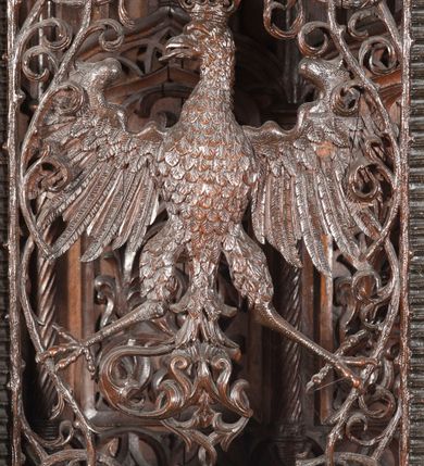 Zdjęcie nr 15: Ołtarz architektoniczny, dwukondygnacyjny ze zwieńczeniem, trójosiowy. Neogotycki na trapezowym postumencie. Mensa wsparta na dwóch  kolumnach o schodkowych, bazach w formie ośmioramiennych gwiazd na siedmiobokach z wklęsłymi ramionami. Z każdego ramienia gwiazd strzeliście unosiła się ku kapitelowi wzdłuż trzonu służka, tworząc u dołu romboidalną, wklęsłą siatkę. Struktura ta zachowała się mniej niż  w połowie na lewej kolumnie. Kapitel lewy ornamentalnie pokryty regularną siatką ze stylizowanych, suchych gałęzi, które tworzą trzy strefy pól ornamentalnych. Dolne przypominają ostre łuki, krzyżują się w nich gałęzie. Środkowe, romboidalne są puste a górne wypełniają sploty suchego akantu. Prawy kapitel posiada podobne podziały pól, różni się wypełnieniem górnej ze stref, gdzie przestrzeń całkowicie zajmują na przemian bujne winne grona oraz pochylające się kłosy zbóż. Zaplecek pod mensą, od frontu podzielono na sześć stref. Na dwóch zewnętrznych i dwóch środkowych znajdują się przedstawienia płaskorzeźbionych łuków okiennych z maswerkami. Druga płaszczyzna od lewej i prawej ozdobiona jest płaskorzeźbą roślinną. Ryzalitowana w części środkowej kondygnacja pierwsza stanowi tabernakulum na cokole. Zadaszenie spadziste pokryte różnorodnym zdobieniem, flankowane czworokątnymi filarami, na których kapitelach wspierają się ramiona ostrych łuków z wimpergami. Powyżej kapitele filarów stanowią blanki z których wyrastają ażurowe formy zbudowane z kilku esownic stylizowane na oset, zakończone profitkami. Widać wnętrze tabernakulum przez ażurowe, dwuskrzydłowe drzwiczki. Na lewych jest przestrzenna rzeźba Orła w koronie osadzona w nieznacznie uszkodzonej oprawie ze splotów gałęzi. Z prawej podobnie wykonane przedstawienie Pogoni Litewskiej. Konny rycerz ma złamany miecz. W centrum ołtarza w prostokątnej ramie znajduje się owalne pole wewnątrz otoczone ciasnym splotem guzowatych gałęzi. W środkowych punktach owalu z gałęzi wstawiono owalne  płaskorzeźby z kości słoniowej ze scenami z życia Chrystusa. W samym środku niewielka rzeźba Jezusa Ukrzyżowanego. Ramę główną flankują postacie Ewangelistów po dwóch z każdej strony, jeden nad drugim, na postumentach i pod gotyckimi baldachimami, najwyższy jest okazalszy. Zwieńczenie ołtarza stanowi wysunięta balustrada zbudowana z ostrołukowych ramion ze sterczynami, centralne ramiona zbiegają się i łączą w sterczynę zakończoną krzyżem. Ołtarz flankowany strzelistymi formami z typowych dla neogotyckiej stylizacji elementami architektonicznymi, w które wkomponowano po jednej postaci świętych z każdej strony.