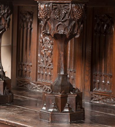 Zdjęcie nr 13: Ołtarz architektoniczny, dwukondygnacyjny ze zwieńczeniem, trójosiowy. Neogotycki na trapezowym postumencie. Mensa wsparta na dwóch  kolumnach o schodkowych, bazach w formie ośmioramiennych gwiazd na siedmiobokach z wklęsłymi ramionami. Z każdego ramienia gwiazd strzeliście unosiła się ku kapitelowi wzdłuż trzonu służka, tworząc u dołu romboidalną, wklęsłą siatkę. Struktura ta zachowała się mniej niż  w połowie na lewej kolumnie. Kapitel lewy ornamentalnie pokryty regularną siatką ze stylizowanych, suchych gałęzi, które tworzą trzy strefy pól ornamentalnych. Dolne przypominają ostre łuki, krzyżują się w nich gałęzie. Środkowe, romboidalne są puste a górne wypełniają sploty suchego akantu. Prawy kapitel posiada podobne podziały pól, różni się wypełnieniem górnej ze stref, gdzie przestrzeń całkowicie zajmują na przemian bujne winne grona oraz pochylające się kłosy zbóż. Zaplecek pod mensą, od frontu podzielono na sześć stref. Na dwóch zewnętrznych i dwóch środkowych znajdują się przedstawienia płaskorzeźbionych łuków okiennych z maswerkami. Druga płaszczyzna od lewej i prawej ozdobiona jest płaskorzeźbą roślinną. Ryzalitowana w części środkowej kondygnacja pierwsza stanowi tabernakulum na cokole. Zadaszenie spadziste pokryte różnorodnym zdobieniem, flankowane czworokątnymi filarami, na których kapitelach wspierają się ramiona ostrych łuków z wimpergami. Powyżej kapitele filarów stanowią blanki z których wyrastają ażurowe formy zbudowane z kilku esownic stylizowane na oset, zakończone profitkami. Widać wnętrze tabernakulum przez ażurowe, dwuskrzydłowe drzwiczki. Na lewych jest przestrzenna rzeźba Orła w koronie osadzona w nieznacznie uszkodzonej oprawie ze splotów gałęzi. Z prawej podobnie wykonane przedstawienie Pogoni Litewskiej. Konny rycerz ma złamany miecz. W centrum ołtarza w prostokątnej ramie znajduje się owalne pole wewnątrz otoczone ciasnym splotem guzowatych gałęzi. W środkowych punktach owalu z gałęzi wstawiono owalne  płaskorzeźby z kości słoniowej ze scenami z życia Chrystusa. W samym środku niewielka rzeźba Jezusa Ukrzyżowanego. Ramę główną flankują postacie Ewangelistów po dwóch z każdej strony, jeden nad drugim, na postumentach i pod gotyckimi baldachimami, najwyższy jest okazalszy. Zwieńczenie ołtarza stanowi wysunięta balustrada zbudowana z ostrołukowych ramion ze sterczynami, centralne ramiona zbiegają się i łączą w sterczynę zakończoną krzyżem. Ołtarz flankowany strzelistymi formami z typowych dla neogotyckiej stylizacji elementami architektonicznymi, w które wkomponowano po jednej postaci świętych z każdej strony.