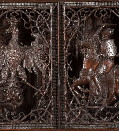 Zdjęcie nr 23: Ołtarz architektoniczny, dwukondygnacyjny ze zwieńczeniem, trójosiowy. Neogotycki na trapezowym postumencie. Mensa wsparta na dwóch  kolumnach o schodkowych, bazach w formie ośmioramiennych gwiazd na siedmiobokach z wklęsłymi ramionami. Z każdego ramienia gwiazd strzeliście unosiła się ku kapitelowi wzdłuż trzonu służka, tworząc u dołu romboidalną, wklęsłą siatkę. Struktura ta zachowała się mniej niż  w połowie na lewej kolumnie. Kapitel lewy ornamentalnie pokryty regularną siatką ze stylizowanych, suchych gałęzi, które tworzą trzy strefy pól ornamentalnych. Dolne przypominają ostre łuki, krzyżują się w nich gałęzie. Środkowe, romboidalne są puste a górne wypełniają sploty suchego akantu. Prawy kapitel posiada podobne podziały pól, różni się wypełnieniem górnej ze stref, gdzie przestrzeń całkowicie zajmują na przemian bujne winne grona oraz pochylające się kłosy zbóż. Zaplecek pod mensą, od frontu podzielono na sześć stref. Na dwóch zewnętrznych i dwóch środkowych znajdują się przedstawienia płaskorzeźbionych łuków okiennych z maswerkami. Druga płaszczyzna od lewej i prawej ozdobiona jest płaskorzeźbą roślinną. Ryzalitowana w części środkowej kondygnacja pierwsza stanowi tabernakulum na cokole. Zadaszenie spadziste pokryte różnorodnym zdobieniem, flankowane czworokątnymi filarami, na których kapitelach wspierają się ramiona ostrych łuków z wimpergami. Powyżej kapitele filarów stanowią blanki z których wyrastają ażurowe formy zbudowane z kilku esownic stylizowane na oset, zakończone profitkami. Widać wnętrze tabernakulum przez ażurowe, dwuskrzydłowe drzwiczki. Na lewych jest przestrzenna rzeźba Orła w koronie osadzona w nieznacznie uszkodzonej oprawie ze splotów gałęzi. Z prawej podobnie wykonane przedstawienie Pogoni Litewskiej. Konny rycerz ma złamany miecz. W centrum ołtarza w prostokątnej ramie znajduje się owalne pole wewnątrz otoczone ciasnym splotem guzowatych gałęzi. W środkowych punktach owalu z gałęzi wstawiono owalne  płaskorzeźby z kości słoniowej ze scenami z życia Chrystusa. W samym środku niewielka rzeźba Jezusa Ukrzyżowanego. Ramę główną flankują postacie Ewangelistów po dwóch z każdej strony, jeden nad drugim, na postumentach i pod gotyckimi baldachimami, najwyższy jest okazalszy. Zwieńczenie ołtarza stanowi wysunięta balustrada zbudowana z ostrołukowych ramion ze sterczynami, centralne ramiona zbiegają się i łączą w sterczynę zakończoną krzyżem. Ołtarz flankowany strzelistymi formami z typowych dla neogotyckiej stylizacji elementami architektonicznymi, w które wkomponowano po jednej postaci świętych z każdej strony.