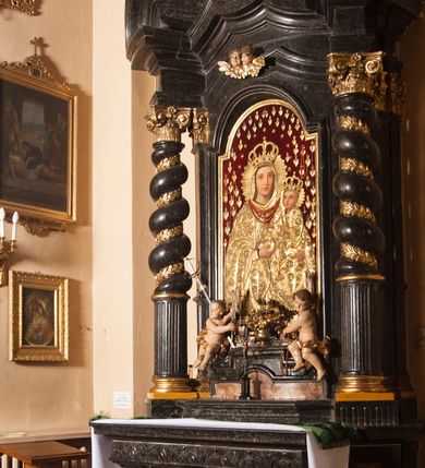 Zdjęcie nr 8: Ołtarz prostopadłościenny, w typie tumbowym, z mensą o brzegu zdobionym rzędem liści akantu naprzemian z łukami kotarowymi zwieńczonymi kulami oraz podwieszonym lambrekinem. Nastawa ołtarzowa jest architektoniczna, jednoosiowa ze zwieńczeniem, ujęta przez kolumny stojące na ukośnie dostawionych cokołach. Kolumny w jednej trzeciej kanelowane w dwóch trzecich skręcone z wplecioną złoconą wicią roślinną, ze złoconym kapitelem podtrzymują przerwany przyczółek ze ślimacznicami, na którym siedzą aniołki. Belkowanie bogato profilowane nad częścią środkową jest wyłamane trzema wklęsłymi łukami. Zwieńczenie jest utworzone z owalnego obrazu z przedstawieniem św. Kingi, w profilowanej ramie ujętej wieńcem z lauru.   

