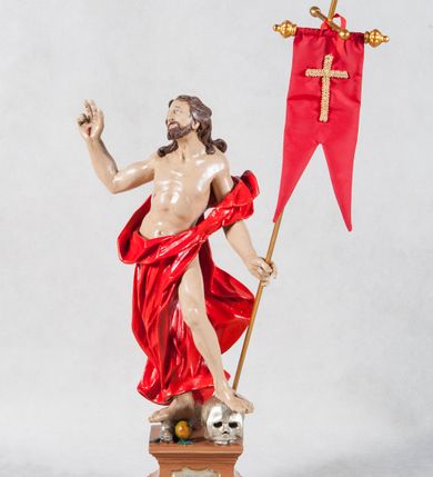Zdjęcie nr 1: Rzeźba Chrystusa Zmartwychwstałego pełna, ustawiona na wysokim, profilowanym cokoliku. Chrystus w ujęciu całopostaciowym, przedstawiony z krzyżem i proporcem, zwrócony lekko w prawo. Ujęty w pozycji stojącej w kontrapoście z ugiętą lewą nogą wspartą na czaszce Adama. Prawą depcze węża trzymającego w pysku jabłko. Twarz owalna, okolona zarostem, włosy długie, zbite w pukle, luźno opadają na ramiona. Na plecy narzucony płaszcz, silnie drapowany na linii bioder i osłaniający prawą nogę. Stopy bose. Na boku korpusu, dłoniach oraz stopach widoczne rany. Jezus prawą rękę ma uniesioną w geście błogosławieństwa, lewą podtrzymuje krzyż i proporzec. 