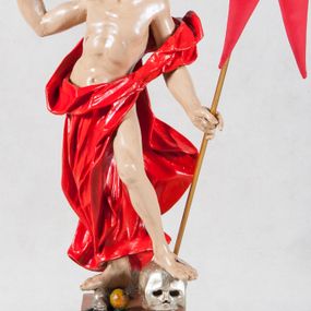 Zdjęcie nr 1: Rzeźba Chrystusa Zmartwychwstałego pełna, ustawiona na wysokim, profilowanym cokoliku. Chrystus w ujęciu całopostaciowym, przedstawiony z krzyżem i proporcem, zwrócony lekko w prawo. Ujęty w pozycji stojącej w kontrapoście z ugiętą lewą nogą wspartą na czaszce Adama. Prawą depcze węża trzymającego w pysku jabłko. Twarz owalna, okolona zarostem, włosy długie, zbite w pukle, luźno opadają na ramiona. Na plecy narzucony płaszcz, silnie drapowany na linii bioder i osłaniający prawą nogę. Stopy bose. Na boku korpusu, dłoniach oraz stopach widoczne rany. Jezus prawą rękę ma uniesioną w geście błogosławieństwa, lewą podtrzymuje krzyż i proporzec. 