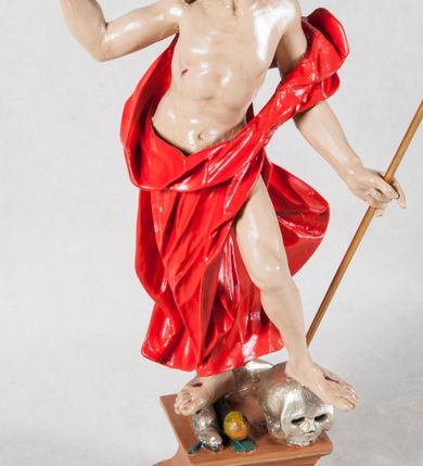 Zdjęcie nr 3: Rzeźba Chrystusa Zmartwychwstałego pełna, ustawiona na wysokim, profilowanym cokoliku. Chrystus w ujęciu całopostaciowym, przedstawiony z krzyżem i proporcem, zwrócony lekko w prawo. Ujęty w pozycji stojącej w kontrapoście z ugiętą lewą nogą wspartą na czaszce Adama. Prawą depcze węża trzymającego w pysku jabłko. Twarz owalna, okolona zarostem, włosy długie, zbite w pukle, luźno opadają na ramiona. Na plecy narzucony płaszcz, silnie drapowany na linii bioder i osłaniający prawą nogę. Stopy bose. Na boku korpusu, dłoniach oraz stopach widoczne rany. Jezus prawą rękę ma uniesioną w geście błogosławieństwa, lewą podtrzymuje krzyż i proporzec. 