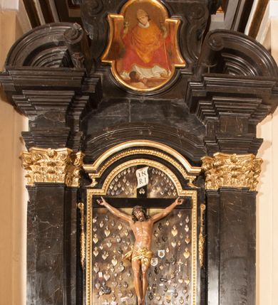 Zdjęcie nr 1: Ołtarz architektoniczny, jednoosiowy, jednokondygnacyjny ze zwieńczeniem. Jego mensa jest w typie tumbowym, antepedium w kształcie płyciny wypełnionej różowym marmurem paczółtowickim, z półkolistymi wcięciami na dłuższych bokach. Nastawa jest ujęta zwielokrotnionymi pilastrami o kompozytowych kapitelach, złoconych, podtrzymujących odcinki belkowania z ćwierćkolistymi naczółkami. Belkowanie połączone w partii architrawu, wygiętego łukowato. Zwieńczenie ujęte spływami wolutowymi, podtrzymującymi gzyms o formie łuku nadwieszonego. W polu środkowym rzeźba Chrystusa na krzyżu, na tle płaskorzeźbionego widoku Jerozolimy, ujętego drewnianą, złoconą ramą w formie stojącego prostokąta, z wyciętą łukowato dolną krawędzią i ściętymi ćwierćkoliście narożami, zwieńczonego podwójnym łukiem półkolistym, nadwieszonym. Na całej powierzchni widoku Jerozolimy ulokowane liczne wota. W zwieńczeniu obraz ze sceną Wskrzeszenia Piotrowina, w fantazyjnie wyciętej ramie o bokach krótszych wybrzuszonych a długich wklęsłych. 

