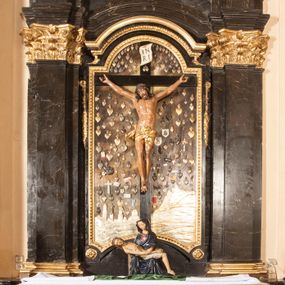 Zdjęcie nr 1: Ołtarz architektoniczny, jednoosiowy, jednokondygnacyjny ze zwieńczeniem. Jego mensa jest w typie tumbowym, antepedium w kształcie płyciny wypełnionej różowym marmurem paczółtowickim, z półkolistymi wcięciami na dłuższych bokach. Nastawa jest ujęta zwielokrotnionymi pilastrami o kompozytowych kapitelach, złoconych, podtrzymujących odcinki belkowania z ćwierćkolistymi naczółkami. Belkowanie połączone w partii architrawu, wygiętego łukowato. Zwieńczenie ujęte spływami wolutowymi, podtrzymującymi gzyms o formie łuku nadwieszonego. W polu środkowym rzeźba Chrystusa na krzyżu, na tle płaskorzeźbionego widoku Jerozolimy, ujętego drewnianą, złoconą ramą w formie stojącego prostokąta, z wyciętą łukowato dolną krawędzią i ściętymi ćwierćkoliście narożami, zwieńczonego podwójnym łukiem półkolistym, nadwieszonym. Na całej powierzchni widoku Jerozolimy ulokowane liczne wota. W zwieńczeniu obraz ze sceną Wskrzeszenia Piotrowina, w fantazyjnie wyciętej ramie o bokach krótszych wybrzuszonych a długich wklęsłych. 

