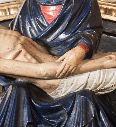 Zdjęcie nr 7: Rzeźba przedstawia siedzącą Marię trzymającą na kolanach ciało swego syna. Maria ustawiona frontalnie, z torsem skręconym lekko w prawo, ubrana w czerwoną suknię i ciemnoniebieski płaszcz z kapturem na głowie. Prawą ręką podtrzymuje syna, a lewą ujmuje go za prawą rękę. Twarz okrągła, pochylona ku Jezusowi, widać na niej boleść; oczy i włosy ciemne, długi nos i zwięzłe usta. Ciało Chrystusa odziane tylko w perizonium spoczywa na kolanach matki, tułów i głowa proste, nogi w kolanach opadają na ziemię, korpus wychudzony tak, że widać żebra i ślady po gwoździach. Głowa w nienaturalnej pozie, prawie w jednej linii z tułowiem, na twarzy widać ból; oczy zamknięte, usta lekko otwarte. Długie do ramion włosy otaczają głowę, lekko zaznaczona broda.