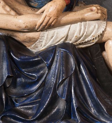Zdjęcie nr 6: Rzeźba przedstawia siedzącą Marię trzymającą na kolanach ciało swego syna. Maria ustawiona frontalnie, z torsem skręconym lekko w prawo, ubrana w czerwoną suknię i ciemnoniebieski płaszcz z kapturem na głowie. Prawą ręką podtrzymuje syna, a lewą ujmuje go za prawą rękę. Twarz okrągła, pochylona ku Jezusowi, widać na niej boleść; oczy i włosy ciemne, długi nos i zwięzłe usta. Ciało Chrystusa odziane tylko w perizonium spoczywa na kolanach matki, tułów i głowa proste, nogi w kolanach opadają na ziemię, korpus wychudzony tak, że widać żebra i ślady po gwoździach. Głowa w nienaturalnej pozie, prawie w jednej linii z tułowiem, na twarzy widać ból; oczy zamknięte, usta lekko otwarte. Długie do ramion włosy otaczają głowę, lekko zaznaczona broda.