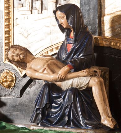 Zdjęcie nr 3: Rzeźba przedstawia siedzącą Marię trzymającą na kolanach ciało swego syna. Maria ustawiona frontalnie, z torsem skręconym lekko w prawo, ubrana w czerwoną suknię i ciemnoniebieski płaszcz z kapturem na głowie. Prawą ręką podtrzymuje syna, a lewą ujmuje go za prawą rękę. Twarz okrągła, pochylona ku Jezusowi, widać na niej boleść; oczy i włosy ciemne, długi nos i zwięzłe usta. Ciało Chrystusa odziane tylko w perizonium spoczywa na kolanach matki, tułów i głowa proste, nogi w kolanach opadają na ziemię, korpus wychudzony tak, że widać żebra i ślady po gwoździach. Głowa w nienaturalnej pozie, prawie w jednej linii z tułowiem, na twarzy widać ból; oczy zamknięte, usta lekko otwarte. Długie do ramion włosy otaczają głowę, lekko zaznaczona broda.