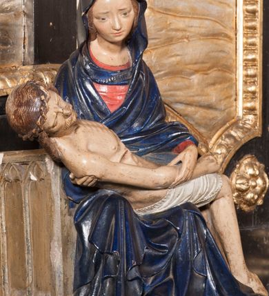 Zdjęcie nr 2: Rzeźba przedstawia siedzącą Marię trzymającą na kolanach ciało swego syna. Maria ustawiona frontalnie, z torsem skręconym lekko w prawo, ubrana w czerwoną suknię i ciemnoniebieski płaszcz z kapturem na głowie. Prawą ręką podtrzymuje syna, a lewą ujmuje go za prawą rękę. Twarz okrągła, pochylona ku Jezusowi, widać na niej boleść; oczy i włosy ciemne, długi nos i zwięzłe usta. Ciało Chrystusa odziane tylko w perizonium spoczywa na kolanach matki, tułów i głowa proste, nogi w kolanach opadają na ziemię, korpus wychudzony tak, że widać żebra i ślady po gwoździach. Głowa w nienaturalnej pozie, prawie w jednej linii z tułowiem, na twarzy widać ból; oczy zamknięte, usta lekko otwarte. Długie do ramion włosy otaczają głowę, lekko zaznaczona broda.