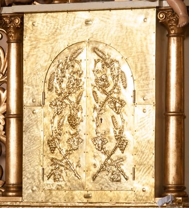 Zdjęcie nr 5: Ołtarz architektoniczny,  przyścienny, trójosiowy, jednokondygnacyjny ze zwieńczeniem. Mensa ołtarzowa kamienna, sarkofagowa, przesłonięta drewnianym antepedium, w centrum którego umieszczono pastorał, krzyż, infułę i księgę w otoczeniu winnej latorośli. Antepedium otoczone ramą ze zdobionymi narożami. Na mensie ustawiono tabernakulum dwukondygnacyjne ze zwieńczeniem, flankowane kolumnami kompozytowymi z pierścieniami w połowie. W dolnej kondygnacji metalowy front z drzwiami o wykroju łuku, zdobionymi splotem kłosów zbóż i kiści winogron. W górnej kondygnacji srebrna płaskorzeźba pelikana karmiącego trzy pisklęta. Po bokach siedzą dwa aniołki. Tabernakulum flankowane stylizowanym przestrzennym ornamentem akantowym. Nastawa posadowiona na wysokim, dekorowanym płycinami, dwudzielnym cokole, którego boczne osie zostały ustawione skośnie w stosunku do głównej. W polu centralnym obraz ze sceną wskrzeszenie Piotrowina przez św. Stanisława w kształcie prostokąta zamkniętego od góry łukiem półkolistym, w złoconej, profilowanej ramie otoczonej srebrnymi orłami oraz stylizowaną wicią roślinną. Powyżej, w zwieńczeniu gloria promienista. W jej centrum Trójca Święta: tronujący wśród obłoków i aniołków Chrystus po lewej stronie i Bóg Ojciec po prawej; powyżej nich unosi się gołębica Ducha Świętego. Otaczająca scenę gloria promienista została skomponowana z wiązek krótszych i dłuższych promieni naprzemiennie srebrnych i złotych, rzadziej rozlokowanych w dolnej części. Boczne osie składają się z ustawionych uskokowo na tle pilastrów par kolumn kompozytowych podtrzymujących rozbudowane, wyłamane na ich osiach belkowanie. Cokoły kolumn są dekorowane płycinami wypełnionymi ornamentem, a między nimi  na konsolach ustawiono figury świętych: Piotra po prawej stronie i Pawła po lewej. Na zewnętrznych częściach belkowania umieszczono woluty, na których posadowiono nagie, przewiązane jedynie złotymi szarfami aniołki wskazujące scenę w glorii. Na wewnętrznych częściach siedzi para większych, ubranych w złoto-czerwone suknie aniołów ukazanych w skręcie, spoglądających we wskazywanym kierunku. 
Ołtarz polichromowany na kolor kremowy, płyciny na ciemnożółty i brązowy, profile również na biało i brązowo; ornamenty, profile, detale oraz kolumny złocone.  
