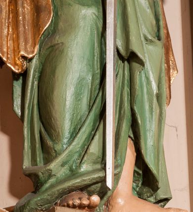 Zdjęcie nr 5: Rzeźba drążona na cokole przedstawiająca św. Pawła ukazanego w całej postaci, zwróconego nieznacznie w lewo. Święty prawą, zgiętą w łokciu ręką trzyma rękojeść opartego o ziemię miecza, lewą podtrzymuje zamkniętą księgę. Ma owalną twarz z dużymi, szeroko otwartymi oczami, prostym nosem oraz wydatnymi ustami; okalają ją ciemnobrązowe, zaczesane do tyłu włosy. Święty ma brodę sięgającą piersi oraz wąsy. Jest ubrany w kremową tunikę z długimi rękawami, zapinaną na guziki i przepasaną w talii oraz zielony płaszcz ze złotym podbiciem przerzucony przez prawe ramię, owijający się wokół bioder i przełożony przez prawą rękę. Tkanina płaszcza spływa do ziemi kaskadowymi fałdami. 
W partiach ciała polichromia naturalistyczna, płaszcz i atrybuty złocone i srebrzone.
