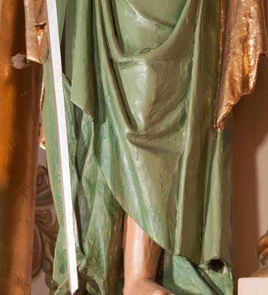 Zdjęcie nr 1: Rzeźba drążona na cokole przedstawiająca św. Pawła ukazanego w całej postaci, zwróconego nieznacznie w lewo. Święty prawą, zgiętą w łokciu ręką trzyma rękojeść opartego o ziemię miecza, lewą podtrzymuje zamkniętą księgę. Ma owalną twarz z dużymi, szeroko otwartymi oczami, prostym nosem oraz wydatnymi ustami; okalają ją ciemnobrązowe, zaczesane do tyłu włosy. Święty ma brodę sięgającą piersi oraz wąsy. Jest ubrany w kremową tunikę z długimi rękawami, zapinaną na guziki i przepasaną w talii oraz zielony płaszcz ze złotym podbiciem przerzucony przez prawe ramię, owijający się wokół bioder i przełożony przez prawą rękę. Tkanina płaszcza spływa do ziemi kaskadowymi fałdami. 
W partiach ciała polichromia naturalistyczna, płaszcz i atrybuty złocone i srebrzone.
