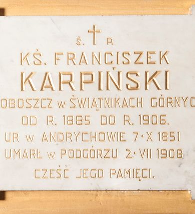 Zdjęcie nr 1: Wmurowana w ścianę kościoła tablica epitafijna w formie leżącego prostokąta z uszakami, na środku których umieszczono metalowe rozetki maskujące miejsca mocowania. Na środku tablicy widnieje złocona inskrypcja „Ś(WIĘTEJ) P(AMIĘCI) / KS(IĄDZ) FRANCISZEK / KARPIŃSKI / PROBOSZCZ W ŚWIĄTNIKACH GÓRNYCH / OD R(OKU) 1885 DO R(OKU) 1906. / UR[ODZONY] W ANDRYCHOWIE 7. X 1851 / UMARŁ W PODGÓRZU 2. VII 1908 / CZEŚĆ JEGO PAMIĘCI”. 