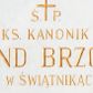 Zdjęcie nr 1: Wmurowana w ścianę kościoła tablica epitafijna w formie leżącego prostokąta z okrągłymi główkami śrub w narożach. Na środku tablicy widnieje złocona inskrypcja „Ś(WIĘTEJ) P(AMIĘCI) / KS(IĄDZ) KANONIK / EDMUND BRZOSTEK / PROBOSZCZ W ŚWIĄTNIKACH GÓRNYCH / OD 1936 R(OKU) DO 1973 R(OKU) / ZA JEGO POSŁUGĘ KAPŁAŃSKĄ / WDZIĘCZNI PARAFIANIE”.