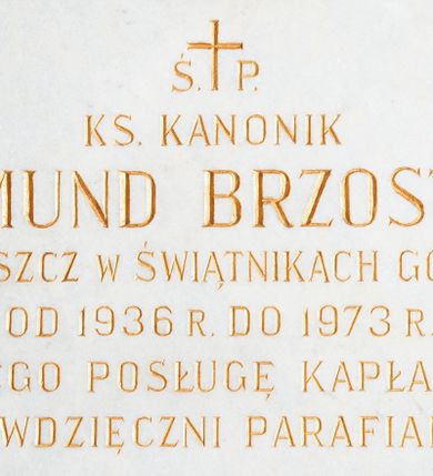 Zdjęcie nr 1: Wmurowana w ścianę kościoła tablica epitafijna w formie leżącego prostokąta z okrągłymi główkami śrub w narożach. Na środku tablicy widnieje złocona inskrypcja „Ś(WIĘTEJ) P(AMIĘCI) / KS(IĄDZ) KANONIK / EDMUND BRZOSTEK / PROBOSZCZ W ŚWIĄTNIKACH GÓRNYCH / OD 1936 R(OKU) DO 1973 R(OKU) / ZA JEGO POSŁUGĘ KAPŁAŃSKĄ / WDZIĘCZNI PARAFIANIE”.