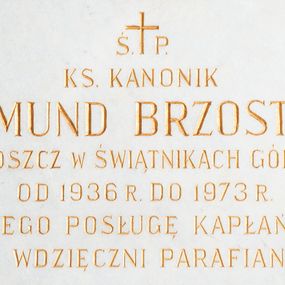 Zdjęcie nr 1: Wmurowana w ścianę kościoła tablica epitafijna w formie leżącego prostokąta z okrągłymi główkami śrub w narożach. Na środku tablicy widnieje złocona inskrypcja „Ś(WIĘTEJ) P(AMIĘCI) / KS(IĄDZ) KANONIK / EDMUND BRZOSTEK / PROBOSZCZ W ŚWIĄTNIKACH GÓRNYCH / OD 1936 R(OKU) DO 1973 R(OKU) / ZA JEGO POSŁUGĘ KAPŁAŃSKĄ / WDZIĘCZNI PARAFIANIE”.