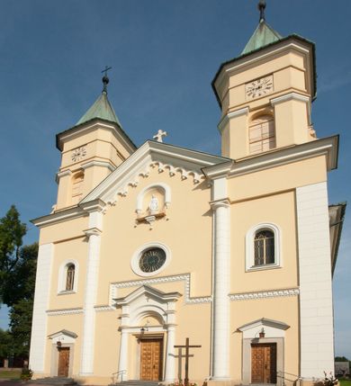 Zdjęcie nr 2: Kościół murowany, trójnawowy, halowy, na rzucie prostokąta z wydłużonym, skierowanym na północ prezbiterium z dobudowaną po zachodniej stronie zakrystią. Prezbiterium jednoprzęsłowe, węższe od korpusu, zamknięte prosto. Nawa główna oraz boczne dwuprzęsłowe, rozdzielone masywnymi opilastrowanymi filarami; artykulacja ścian przy pomocy filarów. Sklepienie prezbiterium kolebkowe, naw żagielkowe, przedzielone gurtami. Od południa chór muzyczny mieszczący się między pierwszymi filarami i powyżej kruchty wejściowej. W prezbiterium jedno okno od wschodu, drugie w zakrystii, w nawach bocznych po dwa. Główne wejście od południa flankowane przez dwa boczne, kolejne do zakrystii i między zakrystią i prezbiterium. Niektóre okna wypełnione gomułkami, ściany i sklepienia kościoła pokrywa polichromia utworzona z dekoracji floralnych i umieszczonych w jej obrębie symboli ewangelistów, herbów i putt wykonujących prace kojarzące się z regionem (bartnicze, ślusarskie, kowalskie itd.). Fasada dwuwieżowa, trójosiowa, dwuprzęsłowa, z portalem na każdej osi. Podziały pionowe przeprowadzono za pomocą półkolumienek i lizen, poziome w formie fryzu kostkowego wyniesionego nad środkowym portalem. Drzwi osi głównej w kształcie stojącego prostokąta ujętego półkolumnami dźwigającymi archiwoltę utworzoną z trzech łuków i trójkątny przyczółek. Drzwi osi bocznych zwieńczone przyczółkami. W drugiej kondygnacji na osi okulus i półokrągła konchowa wnęka z figurą Najświętszego Serca Jezusa poniżej trójkątnego szczytu dekorowanego fryzem arkadkowym. W osiach bocznych okna w kształcie stojącego prostokąta zamkniętego półkoliście. Wyżej dwie kondygnacje wież oddzielone gzymsem, w pierwszej  umieszczono okna, w drugiej tarcze zegarów. Elewacje boczne gładkie, przeprute jedynie oknami. Nawy przykrywa dach dwuspadowy, wieże namiotowe z fartuchem zwieńczone krzyżami.
