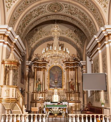 Zdjęcie nr 7: Kościół murowany, trójnawowy, halowy, na rzucie prostokąta z wydłużonym, skierowanym na północ prezbiterium z dobudowaną po zachodniej stronie zakrystią. Prezbiterium jednoprzęsłowe, węższe od korpusu, zamknięte prosto. Nawa główna oraz boczne dwuprzęsłowe, rozdzielone masywnymi opilastrowanymi filarami; artykulacja ścian przy pomocy filarów. Sklepienie prezbiterium kolebkowe, naw żagielkowe, przedzielone gurtami. Od południa chór muzyczny mieszczący się między pierwszymi filarami i powyżej kruchty wejściowej. W prezbiterium jedno okno od wschodu, drugie w zakrystii, w nawach bocznych po dwa. Główne wejście od południa flankowane przez dwa boczne, kolejne do zakrystii i między zakrystią i prezbiterium. Niektóre okna wypełnione gomułkami, ściany i sklepienia kościoła pokrywa polichromia utworzona z dekoracji floralnych i umieszczonych w jej obrębie symboli ewangelistów, herbów i putt wykonujących prace kojarzące się z regionem (bartnicze, ślusarskie, kowalskie itd.). Fasada dwuwieżowa, trójosiowa, dwuprzęsłowa, z portalem na każdej osi. Podziały pionowe przeprowadzono za pomocą półkolumienek i lizen, poziome w formie fryzu kostkowego wyniesionego nad środkowym portalem. Drzwi osi głównej w kształcie stojącego prostokąta ujętego półkolumnami dźwigającymi archiwoltę utworzoną z trzech łuków i trójkątny przyczółek. Drzwi osi bocznych zwieńczone przyczółkami. W drugiej kondygnacji na osi okulus i półokrągła konchowa wnęka z figurą Najświętszego Serca Jezusa poniżej trójkątnego szczytu dekorowanego fryzem arkadkowym. W osiach bocznych okna w kształcie stojącego prostokąta zamkniętego półkoliście. Wyżej dwie kondygnacje wież oddzielone gzymsem, w pierwszej  umieszczono okna, w drugiej tarcze zegarów. Elewacje boczne gładkie, przeprute jedynie oknami. Nawy przykrywa dach dwuspadowy, wieże namiotowe z fartuchem zwieńczone krzyżami.