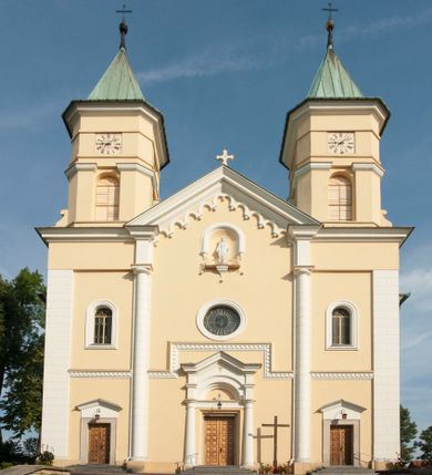 Zdjęcie nr 1: Kościół murowany, trójnawowy, halowy, na rzucie prostokąta z wydłużonym, skierowanym na północ prezbiterium z dobudowaną po zachodniej stronie zakrystią. Prezbiterium jednoprzęsłowe, węższe od korpusu, zamknięte prosto. Nawa główna oraz boczne dwuprzęsłowe, rozdzielone masywnymi opilastrowanymi filarami; artykulacja ścian przy pomocy filarów. Sklepienie prezbiterium kolebkowe, naw żagielkowe, przedzielone gurtami. Od południa chór muzyczny mieszczący się między pierwszymi filarami i powyżej kruchty wejściowej. W prezbiterium jedno okno od wschodu, drugie w zakrystii, w nawach bocznych po dwa. Główne wejście od południa flankowane przez dwa boczne, kolejne do zakrystii i między zakrystią i prezbiterium. Niektóre okna wypełnione gomułkami, ściany i sklepienia kościoła pokrywa polichromia utworzona z dekoracji floralnych i umieszczonych w jej obrębie symboli ewangelistów, herbów i putt wykonujących prace kojarzące się z regionem (bartnicze, ślusarskie, kowalskie itd.). Fasada dwuwieżowa, trójosiowa, dwuprzęsłowa, z portalem na każdej osi. Podziały pionowe przeprowadzono za pomocą półkolumienek i lizen, poziome w formie fryzu kostkowego wyniesionego nad środkowym portalem. Drzwi osi głównej w kształcie stojącego prostokąta ujętego półkolumnami dźwigającymi archiwoltę utworzoną z trzech łuków i trójkątny przyczółek. Drzwi osi bocznych zwieńczone przyczółkami. W drugiej kondygnacji na osi okulus i półokrągła konchowa wnęka z figurą Najświętszego Serca Jezusa poniżej trójkątnego szczytu dekorowanego fryzem arkadkowym. W osiach bocznych okna w kształcie stojącego prostokąta zamkniętego półkoliście. Wyżej dwie kondygnacje wież oddzielone gzymsem, w pierwszej  umieszczono okna, w drugiej tarcze zegarów. Elewacje boczne gładkie, przeprute jedynie oknami. Nawy przykrywa dach dwuspadowy, wieże namiotowe z fartuchem zwieńczone krzyżami.