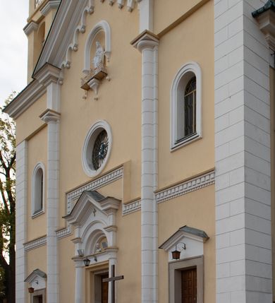 Zdjęcie nr 18: Kościół murowany, trójnawowy, halowy, na rzucie prostokąta z wydłużonym, skierowanym na północ prezbiterium z dobudowaną po zachodniej stronie zakrystią. Prezbiterium jednoprzęsłowe, węższe od korpusu, zamknięte prosto. Nawa główna oraz boczne dwuprzęsłowe, rozdzielone masywnymi opilastrowanymi filarami; artykulacja ścian przy pomocy filarów. Sklepienie prezbiterium kolebkowe, naw żagielkowe, przedzielone gurtami. Od południa chór muzyczny mieszczący się między pierwszymi filarami i powyżej kruchty wejściowej. W prezbiterium jedno okno od wschodu, drugie w zakrystii, w nawach bocznych po dwa. Główne wejście od południa flankowane przez dwa boczne, kolejne do zakrystii i między zakrystią i prezbiterium. Niektóre okna wypełnione gomułkami, ściany i sklepienia kościoła pokrywa polichromia utworzona z dekoracji floralnych i umieszczonych w jej obrębie symboli ewangelistów, herbów i putt wykonujących prace kojarzące się z regionem (bartnicze, ślusarskie, kowalskie itd.). Fasada dwuwieżowa, trójosiowa, dwuprzęsłowa, z portalem na każdej osi. Podziały pionowe przeprowadzono za pomocą półkolumienek i lizen, poziome w formie fryzu kostkowego wyniesionego nad środkowym portalem. Drzwi osi głównej w kształcie stojącego prostokąta ujętego półkolumnami dźwigającymi archiwoltę utworzoną z trzech łuków i trójkątny przyczółek. Drzwi osi bocznych zwieńczone przyczółkami. W drugiej kondygnacji na osi okulus i półokrągła konchowa wnęka z figurą Najświętszego Serca Jezusa poniżej trójkątnego szczytu dekorowanego fryzem arkadkowym. W osiach bocznych okna w kształcie stojącego prostokąta zamkniętego półkoliście. Wyżej dwie kondygnacje wież oddzielone gzymsem, w pierwszej  umieszczono okna, w drugiej tarcze zegarów. Elewacje boczne gładkie, przeprute jedynie oknami. Nawy przykrywa dach dwuspadowy, wieże namiotowe z fartuchem zwieńczone krzyżami.