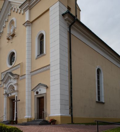 Zdjęcie nr 19: Kościół murowany, trójnawowy, halowy, na rzucie prostokąta z wydłużonym, skierowanym na północ prezbiterium z dobudowaną po zachodniej stronie zakrystią. Prezbiterium jednoprzęsłowe, węższe od korpusu, zamknięte prosto. Nawa główna oraz boczne dwuprzęsłowe, rozdzielone masywnymi opilastrowanymi filarami; artykulacja ścian przy pomocy filarów. Sklepienie prezbiterium kolebkowe, naw żagielkowe, przedzielone gurtami. Od południa chór muzyczny mieszczący się między pierwszymi filarami i powyżej kruchty wejściowej. W prezbiterium jedno okno od wschodu, drugie w zakrystii, w nawach bocznych po dwa. Główne wejście od południa flankowane przez dwa boczne, kolejne do zakrystii i między zakrystią i prezbiterium. Niektóre okna wypełnione gomułkami, ściany i sklepienia kościoła pokrywa polichromia utworzona z dekoracji floralnych i umieszczonych w jej obrębie symboli ewangelistów, herbów i putt wykonujących prace kojarzące się z regionem (bartnicze, ślusarskie, kowalskie itd.). Fasada dwuwieżowa, trójosiowa, dwuprzęsłowa, z portalem na każdej osi. Podziały pionowe przeprowadzono za pomocą półkolumienek i lizen, poziome w formie fryzu kostkowego wyniesionego nad środkowym portalem. Drzwi osi głównej w kształcie stojącego prostokąta ujętego półkolumnami dźwigającymi archiwoltę utworzoną z trzech łuków i trójkątny przyczółek. Drzwi osi bocznych zwieńczone przyczółkami. W drugiej kondygnacji na osi okulus i półokrągła konchowa wnęka z figurą Najświętszego Serca Jezusa poniżej trójkątnego szczytu dekorowanego fryzem arkadkowym. W osiach bocznych okna w kształcie stojącego prostokąta zamkniętego półkoliście. Wyżej dwie kondygnacje wież oddzielone gzymsem, w pierwszej  umieszczono okna, w drugiej tarcze zegarów. Elewacje boczne gładkie, przeprute jedynie oknami. Nawy przykrywa dach dwuspadowy, wieże namiotowe z fartuchem zwieńczone krzyżami.