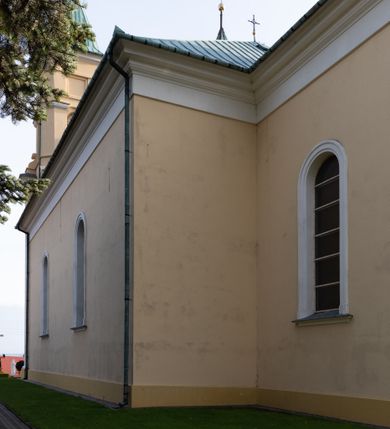 Zdjęcie nr 24: Kościół murowany, trójnawowy, halowy, na rzucie prostokąta z wydłużonym, skierowanym na północ prezbiterium z dobudowaną po zachodniej stronie zakrystią. Prezbiterium jednoprzęsłowe, węższe od korpusu, zamknięte prosto. Nawa główna oraz boczne dwuprzęsłowe, rozdzielone masywnymi opilastrowanymi filarami; artykulacja ścian przy pomocy filarów. Sklepienie prezbiterium kolebkowe, naw żagielkowe, przedzielone gurtami. Od południa chór muzyczny mieszczący się między pierwszymi filarami i powyżej kruchty wejściowej. W prezbiterium jedno okno od wschodu, drugie w zakrystii, w nawach bocznych po dwa. Główne wejście od południa flankowane przez dwa boczne, kolejne do zakrystii i między zakrystią i prezbiterium. Niektóre okna wypełnione gomułkami, ściany i sklepienia kościoła pokrywa polichromia utworzona z dekoracji floralnych i umieszczonych w jej obrębie symboli ewangelistów, herbów i putt wykonujących prace kojarzące się z regionem (bartnicze, ślusarskie, kowalskie itd.). Fasada dwuwieżowa, trójosiowa, dwuprzęsłowa, z portalem na każdej osi. Podziały pionowe przeprowadzono za pomocą półkolumienek i lizen, poziome w formie fryzu kostkowego wyniesionego nad środkowym portalem. Drzwi osi głównej w kształcie stojącego prostokąta ujętego półkolumnami dźwigającymi archiwoltę utworzoną z trzech łuków i trójkątny przyczółek. Drzwi osi bocznych zwieńczone przyczółkami. W drugiej kondygnacji na osi okulus i półokrągła konchowa wnęka z figurą Najświętszego Serca Jezusa poniżej trójkątnego szczytu dekorowanego fryzem arkadkowym. W osiach bocznych okna w kształcie stojącego prostokąta zamkniętego półkoliście. Wyżej dwie kondygnacje wież oddzielone gzymsem, w pierwszej  umieszczono okna, w drugiej tarcze zegarów. Elewacje boczne gładkie, przeprute jedynie oknami. Nawy przykrywa dach dwuspadowy, wieże namiotowe z fartuchem zwieńczone krzyżami.
