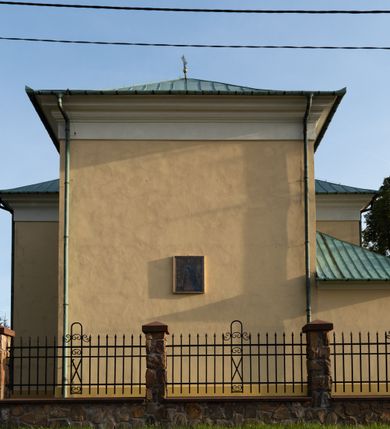 Zdjęcie nr 26: Kościół murowany, trójnawowy, halowy, na rzucie prostokąta z wydłużonym, skierowanym na północ prezbiterium z dobudowaną po zachodniej stronie zakrystią. Prezbiterium jednoprzęsłowe, węższe od korpusu, zamknięte prosto. Nawa główna oraz boczne dwuprzęsłowe, rozdzielone masywnymi opilastrowanymi filarami; artykulacja ścian przy pomocy filarów. Sklepienie prezbiterium kolebkowe, naw żagielkowe, przedzielone gurtami. Od południa chór muzyczny mieszczący się między pierwszymi filarami i powyżej kruchty wejściowej. W prezbiterium jedno okno od wschodu, drugie w zakrystii, w nawach bocznych po dwa. Główne wejście od południa flankowane przez dwa boczne, kolejne do zakrystii i między zakrystią i prezbiterium. Niektóre okna wypełnione gomułkami, ściany i sklepienia kościoła pokrywa polichromia utworzona z dekoracji floralnych i umieszczonych w jej obrębie symboli ewangelistów, herbów i putt wykonujących prace kojarzące się z regionem (bartnicze, ślusarskie, kowalskie itd.). Fasada dwuwieżowa, trójosiowa, dwuprzęsłowa, z portalem na każdej osi. Podziały pionowe przeprowadzono za pomocą półkolumienek i lizen, poziome w formie fryzu kostkowego wyniesionego nad środkowym portalem. Drzwi osi głównej w kształcie stojącego prostokąta ujętego półkolumnami dźwigającymi archiwoltę utworzoną z trzech łuków i trójkątny przyczółek. Drzwi osi bocznych zwieńczone przyczółkami. W drugiej kondygnacji na osi okulus i półokrągła konchowa wnęka z figurą Najświętszego Serca Jezusa poniżej trójkątnego szczytu dekorowanego fryzem arkadkowym. W osiach bocznych okna w kształcie stojącego prostokąta zamkniętego półkoliście. Wyżej dwie kondygnacje wież oddzielone gzymsem, w pierwszej  umieszczono okna, w drugiej tarcze zegarów. Elewacje boczne gładkie, przeprute jedynie oknami. Nawy przykrywa dach dwuspadowy, wieże namiotowe z fartuchem zwieńczone krzyżami.