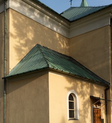 Zdjęcie nr 28: Kościół murowany, trójnawowy, halowy, na rzucie prostokąta z wydłużonym, skierowanym na północ prezbiterium z dobudowaną po zachodniej stronie zakrystią. Prezbiterium jednoprzęsłowe, węższe od korpusu, zamknięte prosto. Nawa główna oraz boczne dwuprzęsłowe, rozdzielone masywnymi opilastrowanymi filarami; artykulacja ścian przy pomocy filarów. Sklepienie prezbiterium kolebkowe, naw żagielkowe, przedzielone gurtami. Od południa chór muzyczny mieszczący się między pierwszymi filarami i powyżej kruchty wejściowej. W prezbiterium jedno okno od wschodu, drugie w zakrystii, w nawach bocznych po dwa. Główne wejście od południa flankowane przez dwa boczne, kolejne do zakrystii i między zakrystią i prezbiterium. Niektóre okna wypełnione gomułkami, ściany i sklepienia kościoła pokrywa polichromia utworzona z dekoracji floralnych i umieszczonych w jej obrębie symboli ewangelistów, herbów i putt wykonujących prace kojarzące się z regionem (bartnicze, ślusarskie, kowalskie itd.). Fasada dwuwieżowa, trójosiowa, dwuprzęsłowa, z portalem na każdej osi. Podziały pionowe przeprowadzono za pomocą półkolumienek i lizen, poziome w formie fryzu kostkowego wyniesionego nad środkowym portalem. Drzwi osi głównej w kształcie stojącego prostokąta ujętego półkolumnami dźwigającymi archiwoltę utworzoną z trzech łuków i trójkątny przyczółek. Drzwi osi bocznych zwieńczone przyczółkami. W drugiej kondygnacji na osi okulus i półokrągła konchowa wnęka z figurą Najświętszego Serca Jezusa poniżej trójkątnego szczytu dekorowanego fryzem arkadkowym. W osiach bocznych okna w kształcie stojącego prostokąta zamkniętego półkoliście. Wyżej dwie kondygnacje wież oddzielone gzymsem, w pierwszej  umieszczono okna, w drugiej tarcze zegarów. Elewacje boczne gładkie, przeprute jedynie oknami. Nawy przykrywa dach dwuspadowy, wieże namiotowe z fartuchem zwieńczone krzyżami.