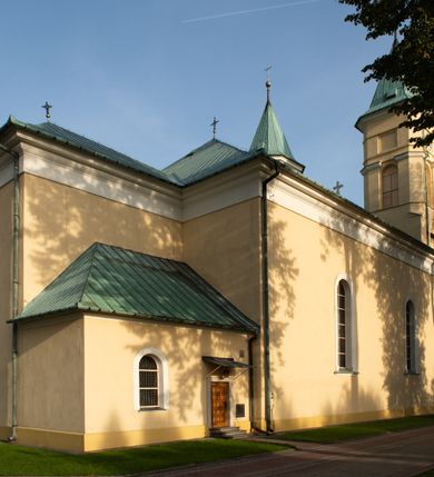 Zdjęcie nr 29: Kościół murowany, trójnawowy, halowy, na rzucie prostokąta z wydłużonym, skierowanym na północ prezbiterium z dobudowaną po zachodniej stronie zakrystią. Prezbiterium jednoprzęsłowe, węższe od korpusu, zamknięte prosto. Nawa główna oraz boczne dwuprzęsłowe, rozdzielone masywnymi opilastrowanymi filarami; artykulacja ścian przy pomocy filarów. Sklepienie prezbiterium kolebkowe, naw żagielkowe, przedzielone gurtami. Od południa chór muzyczny mieszczący się między pierwszymi filarami i powyżej kruchty wejściowej. W prezbiterium jedno okno od wschodu, drugie w zakrystii, w nawach bocznych po dwa. Główne wejście od południa flankowane przez dwa boczne, kolejne do zakrystii i między zakrystią i prezbiterium. Niektóre okna wypełnione gomułkami, ściany i sklepienia kościoła pokrywa polichromia utworzona z dekoracji floralnych i umieszczonych w jej obrębie symboli ewangelistów, herbów i putt wykonujących prace kojarzące się z regionem (bartnicze, ślusarskie, kowalskie itd.). Fasada dwuwieżowa, trójosiowa, dwuprzęsłowa, z portalem na każdej osi. Podziały pionowe przeprowadzono za pomocą półkolumienek i lizen, poziome w formie fryzu kostkowego wyniesionego nad środkowym portalem. Drzwi osi głównej w kształcie stojącego prostokąta ujętego półkolumnami dźwigającymi archiwoltę utworzoną z trzech łuków i trójkątny przyczółek. Drzwi osi bocznych zwieńczone przyczółkami. W drugiej kondygnacji na osi okulus i półokrągła konchowa wnęka z figurą Najświętszego Serca Jezusa poniżej trójkątnego szczytu dekorowanego fryzem arkadkowym. W osiach bocznych okna w kształcie stojącego prostokąta zamkniętego półkoliście. Wyżej dwie kondygnacje wież oddzielone gzymsem, w pierwszej  umieszczono okna, w drugiej tarcze zegarów. Elewacje boczne gładkie, przeprute jedynie oknami. Nawy przykrywa dach dwuspadowy, wieże namiotowe z fartuchem zwieńczone krzyżami.