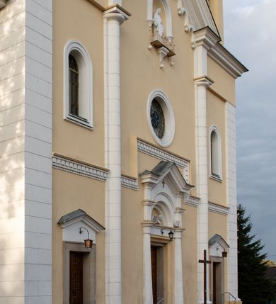 Zdjęcie nr 32: Kościół murowany, trójnawowy, halowy, na rzucie prostokąta z wydłużonym, skierowanym na północ prezbiterium z dobudowaną po zachodniej stronie zakrystią. Prezbiterium jednoprzęsłowe, węższe od korpusu, zamknięte prosto. Nawa główna oraz boczne dwuprzęsłowe, rozdzielone masywnymi opilastrowanymi filarami; artykulacja ścian przy pomocy filarów. Sklepienie prezbiterium kolebkowe, naw żagielkowe, przedzielone gurtami. Od południa chór muzyczny mieszczący się między pierwszymi filarami i powyżej kruchty wejściowej. W prezbiterium jedno okno od wschodu, drugie w zakrystii, w nawach bocznych po dwa. Główne wejście od południa flankowane przez dwa boczne, kolejne do zakrystii i między zakrystią i prezbiterium. Niektóre okna wypełnione gomułkami, ściany i sklepienia kościoła pokrywa polichromia utworzona z dekoracji floralnych i umieszczonych w jej obrębie symboli ewangelistów, herbów i putt wykonujących prace kojarzące się z regionem (bartnicze, ślusarskie, kowalskie itd.). Fasada dwuwieżowa, trójosiowa, dwuprzęsłowa, z portalem na każdej osi. Podziały pionowe przeprowadzono za pomocą półkolumienek i lizen, poziome w formie fryzu kostkowego wyniesionego nad środkowym portalem. Drzwi osi głównej w kształcie stojącego prostokąta ujętego półkolumnami dźwigającymi archiwoltę utworzoną z trzech łuków i trójkątny przyczółek. Drzwi osi bocznych zwieńczone przyczółkami. W drugiej kondygnacji na osi okulus i półokrągła konchowa wnęka z figurą Najświętszego Serca Jezusa poniżej trójkątnego szczytu dekorowanego fryzem arkadkowym. W osiach bocznych okna w kształcie stojącego prostokąta zamkniętego półkoliście. Wyżej dwie kondygnacje wież oddzielone gzymsem, w pierwszej  umieszczono okna, w drugiej tarcze zegarów. Elewacje boczne gładkie, przeprute jedynie oknami. Nawy przykrywa dach dwuspadowy, wieże namiotowe z fartuchem zwieńczone krzyżami.