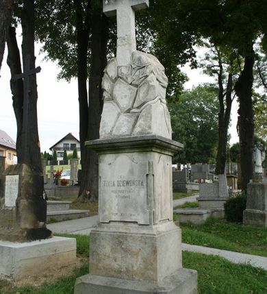 Zdjęcie nr 2: Nagrobek wolnostojący złożony z cokołu na dwustopniowej podstawie, na którym posadowiono rzeźbę zwieńczoną krzyżem. Podstawa gładka, dolna część szersza i niższa niż górna. Cokół zwieńczony wydatnym, profilowanym gzymsem. Na jego frontowej ścianie, na tablicy w kształcie stojącego prostokąta zamkniętego od góry łukiem nadwieszonym, z uszakami w narożach dwa miejsca na medaliony oraz inskrypcja „Ś(WIĘTEJ) P(AMIĘCI) / STEFAN DZIEWOŃSKI / 1871 + 19/9 1903 / STANISŁAW DZIEWOŃSKI / *1860 +22/11 1907 / SYNOWIE”. 
Z tyłu nagrobka „Ś(WIĘTEJ) P(AMIĘCI) / TEKLA DZIEWOŃSKA / PRZEŻYWSZY LAT 76. / +31/7 1907. / SPOKÓJ ICH DUSZOM”. Na cokole ustawiono rzeźbę zrozpaczonej kobiety, która siedzi na skałach, głowę składa na lewej ręce opartej o kamień, w prawej trzyma rozwinięte róże. Spod bogato marszczonej sukni z krótkimi rękawami wystaje goła stopa; na głowie welon opadający na plecy. Z tyłu rzeźba imituje ułożone na sobie kamienie. Kompozycję wieńczy gładki krzyż łaciński. 