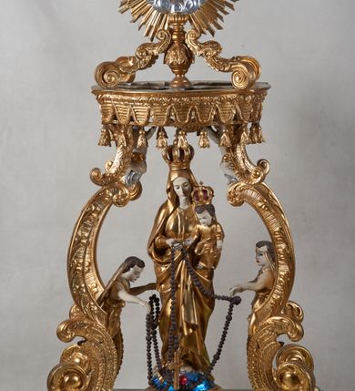 Zdjęcie nr 2: Na profilowanym, prostopadłościennym postumencie ustawiona pełnoplastyczna figura Matki Boskiej z Dzieciątkiem stojącej na niebieskim globie ziemskim, depczącej węża z czerwonym jabłkiem w pysku i podtrzymującej  różaniec. Maria jest ubrana w długie, złocone szaty, na lewym ręku podtrzymuje analogicznie ubrane Dzieciątko. Obie postaci w koronach zamkniętych. Po bokach i na górze pełnoplastyczne wizerunki aniołków siedzących na obłokach i podtrzymujących części różańca oraz różany wieniec nad głową Marii. Całość otoczona ażurową strukturą utworzoną z esowato akantowo-rocaille&#039;owych wygiętych wolut, na których ustawiony jest bogato dekorowany lambrekinem baldachim. W zwieńczeniu gloria promienista z monogramem maryjnym w obłokach. Odsłonięte partie ciała postaci polichromowane naturalistycznie, pozostałe fragmenty srebrzone i złocone; postument w kolorze jasnozielonym ze złoconymi profilami.