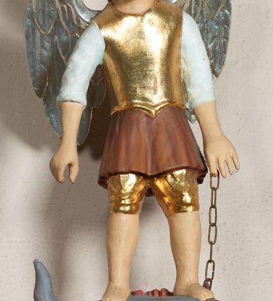 Zdjęcie nr 1: Pełnoplastyczna, polichromowana figura św. Michała Archanioła depczącego smoka. Święty ukazany w pozycji stojącej, z głową przechyloną nieznacznie na prawo. Ma pociągłą twarz o łagodnym wyrazie, niebieskie oczy, szeroki nos i usta. Został przedstawiony w stroju legionisty rzymskiego: w złotym napierśniku, krótkiej, brązowej tunice z białymi, podwiniętymi rękawami oraz złoconym hełmie. W lewej ręce trzyma łańcuch, a na nim smoka pod postacią szarej jaszczurki z ludzką głową i rękami, która leży na zielonej trawie. Polichromia w partiach ciała naturalistyczna, skrzydła srebrzone.