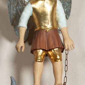 Zdjęcie nr 1: Pełnoplastyczna, polichromowana figura św. Michała Archanioła depczącego smoka. Święty ukazany w pozycji stojącej, z głową przechyloną nieznacznie na prawo. Ma pociągłą twarz o łagodnym wyrazie, niebieskie oczy, szeroki nos i usta. Został przedstawiony w stroju legionisty rzymskiego: w złotym napierśniku, krótkiej, brązowej tunice z białymi, podwiniętymi rękawami oraz złoconym hełmie. W lewej ręce trzyma łańcuch, a na nim smoka pod postacią szarej jaszczurki z ludzką głową i rękami, która leży na zielonej trawie. Polichromia w partiach ciała naturalistyczna, skrzydła srebrzone.