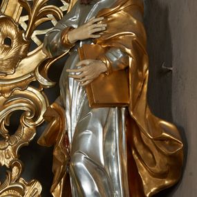Zdjęcie nr 1: Rzeźba pełna, ustawiona frontalnie, o esowatym układzie ciała. Prawa ręka świętego spoczywa na piersi, przytrzymując płaszcz, lewa ugięta, trzyma księgę na lewym biodrze. Głowę ma zwróconą w trzech czwartych w prawo, twarz podłużną, mały nos, wyraźnie otwarte oczy i delikatnie rozchylone usta; okoloną zarostem w postaci długiej brody spływającej na pierś; włosy krótkie, w formie loków. Święty jest ubrany w obficie marszczoną tunikę, ściśle przylegającą do ciała, która spływa w dół w postaci prostych, głęboko rzeźbionych fałd. Płaszcz zawieszony na lewym ramieniu otacza postać, zawijając się na prawym udzie; tkanina ekspresyjnie poruszona, silnie łamana, drapowana w gęste fałdy. Polichromia naturalistyczna w partiach ciała, tunika srebrzona, płaszcz i księga złocone.