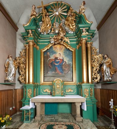 Zdjęcie nr 4: Rzeźba pełna, ustawiona frontalnie, o esowatym układzie ciała. Święty ciężar opiera na lewej nodze, prawą ma ugiętą, opartą na fragmencie skały. Lewą rękę unosi w górę, w stronę ołtarza, w wymownym geście dłoni; prawą ma opuszczoną wzdłuż boku, przytrzymuje księgę. Głowa zwrócona w trzech czwartych w lewo, uniesiona silnie w górę. Twarz podłużna o wyraźnych, głęboko rzeźbionych rysach, wąskim nosie, szeroko otwartych, dużych oczach skierowanych w górę; okolona zarostem; włosy krótkie, delikatnie falowane, opadają na tył głowy. Postać ubrana jest w tunikę przepasaną w talii; tkanina jest silnie drapowana, ściśle przylega do ciała, odzwierciedlając jego układ, opadając w dół w formie gęstych fałd. Święty ma płaszcz przewieszony przez lewe ramię, spływa na plecy w formie ciężkiej, silnie drapowanej i łamanej tkaniny. Polichromia naturalistyczna w partiach ciała, tunika srebrzona, płaszcz oraz księga złocone.