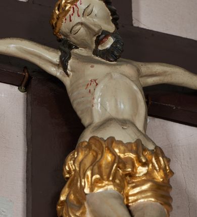 Zdjęcie nr 2: W centrum postać zmarłego Chrystusa, przybitego trzema gwoździami do krzyża. Postać w delikatnym zwisie, o szeroko rozłożonych ramionach i delikatnie przegiętej sylwetce. Duża głowa w koronie cierniowej opada na prawe ramię; twarz o sumarycznych rysach, okolona zarostem; włosy w postaci pukli opadają na ramię. Ciało naprężone, wychudzone, ekspresyjnie kształtowane, uwypuklone poszczególne elementy anatomiczne, z zaznaczonymi śladami męki. Perizonium w formie tkaniny ściśle opasującej biodra, drapowanej w spływające faliście fałdy, ze zwisem na prawym boku. Titulus w formie banderoli z napisem „INRI”.Po lewej stronie figura św. Elżbiety, zwróconej frontalnie z wyciągniętymi przed siebie rękami. Twarz pełna, niezindywidualizowana. Na nakrytej welonem głowie ma koronę. Postać ubrana w błękitną tunikę przepasaną w talii złotą szarfą i podwikę; na ramiona ma narzucony czerwony płaszcz. Po prawej postać św. Katarzyny Sieneńskiej w analogicznym układzie ciała. Twarz pełna, również niezindywidualizowana. Święta jest ubrana w habit dominikański. Karnacja postaci bardzo jasna. 